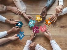several pairs of hands holding puzzle pieces on a wooden table