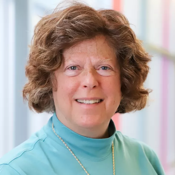 Headshot of Dr. Simpson. Dr. Simpson has red, curly hair. She is wearing a blue turtleneck sweater.