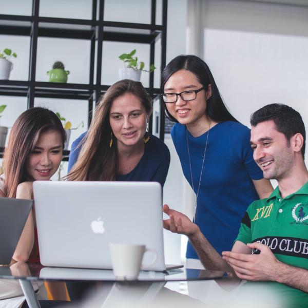 a group of 4 students looking at a laptop, smiling